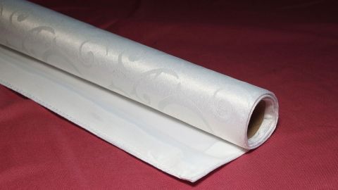 Eine gerollte Tischdecke liegt auf einem roten Untergrund, bereit zum Lagern und späteren Gebrauch.