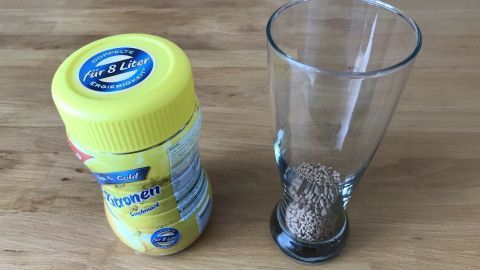 Ein Glas steht neben einem Gelbkapsel-Behälter mit Krümeltee, bereit zur Zubereitung von Eistee mit Korn.