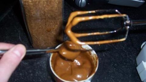 Ein Handmixer schlägt cremigen Kaffee in einer Tasse auf einer schwarzen Küchenarbeitsplatte auf.