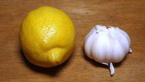 Eine frische Zitrone und eine Knoblauchzehe liegen auf einem Holzuntergrund, bereit für ein gesundes Zitronenknoblauchgetränk.