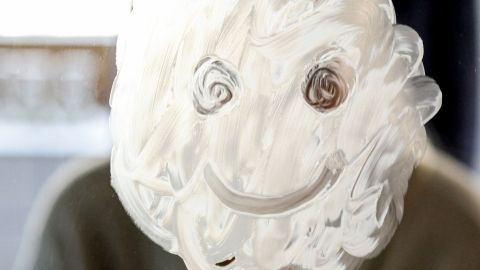 Ein Gesicht aus Schaum ist auf einem Spiegel gemalt, während jemand im Hintergrund entspannt sitzt.