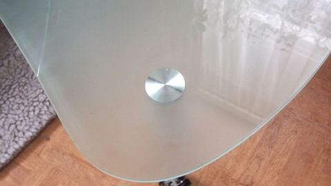 Kratzer auf Milchglas (Opalglas) entfernen, mithilfe von Metallpolisch (Paste) oder Stahlfix (Milch). Ein transparentes Milchglas zeigt einen runden, silbernen Fuß in einem hellen Raum mit Holzfußboden und Teppich.