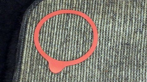 Ein roter Gummiring liegt auf einem rutschenden Teppich und könnte dabei helfen, ihn zu fixieren oder zu stoppen.