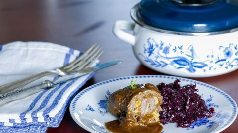 Ein Teller mit Rinderroulade, überzogen mit süßem Senf, liegt neben einem Behälter und Beilagen wie Rotkohl.