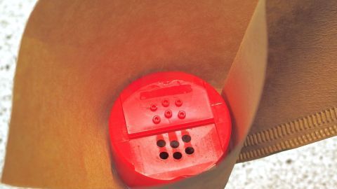 Ein roter Gewürzstreuer wird in eine braune Papiertüte gefüllt, um ihn sicher zu transportieren.