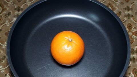 Eine orangefarbene Orange liegt in einer schwarzen Pfanne auf einem gemusterten Untergrund.