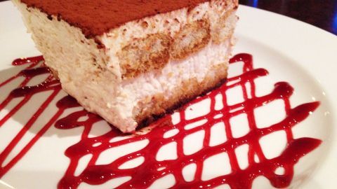 Ein Stück Tiramisu liegt auf einem Teller, umgeben von roter Sauce und zeigt eine verführerische, cremige Textur.