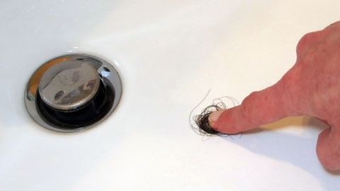 Ein Finger berührt ein verstopftes Abflussloch in einer Badewanne, um Haare zu entfernen, die die Verstopfung verursachen.