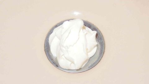 Ein Teller mit einer cremigen Paste liegt in einem Waschbecken, während das Wasser langsam abläuft und Haare im Abfluss vermutet werden.