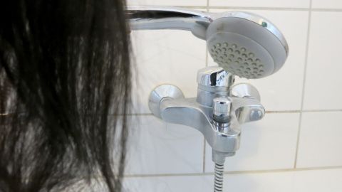 Lange, glänzende Haare fließen über einen Wasserhahn, während kaltes Wasser aus der Duschbrause strömt, um die Haare zu spülen.