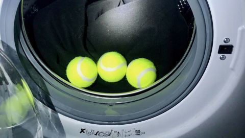 Du kannst Tennisbälle als Waschkugeln verwenden! Gib einfach 3-4 mit in die Trommel. Drei Tennisbälle liegen in einer Waschmaschine, während schwarze Kleidung im Inneren gewaschen wird.