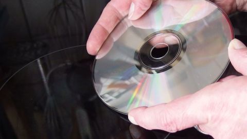 Ein CD wird verwendet, um ein Glaskeramikfeld zu reinigen, während Hände gut sichtbar sind, auf dem schwarzen Untergrund.