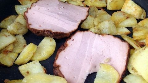 Bratenstücke liegen gebräunt auf einem Bett aus goldenen Kartoffelstücken in einer Pfanne.