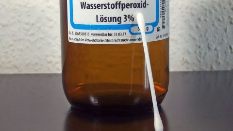 Eine Flasche mit Wasserstoffperoxid steht auf dem Tisch, während ein Wattestäbchen bereit ist, für die Anwendung.