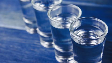Vier klare Wodkagläser stehen auf einem blauen Tisch, bereit zum Anstoßen in geselliger Runde.