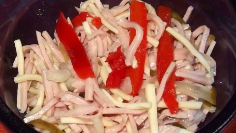Ein bunter Schwäbischer Wurstsalat liegt in einer Schale, gefüllt mit feinen Wurststücken und roten Paprika.