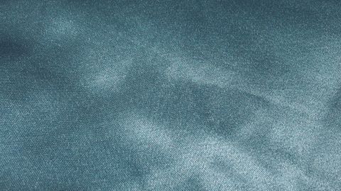 Ein schimmerndes Seidentuch liegt flach und zeigt feine, glatte Texturen in einem sanften, bläulichen Farbton.