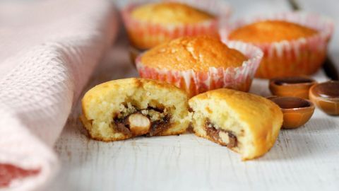 Goldene Muffins sind auf einem weißen Holzbrett angeordnet, mit einem aufgeschnittenen Muffin, der Toffifee-Füllung zeigt.