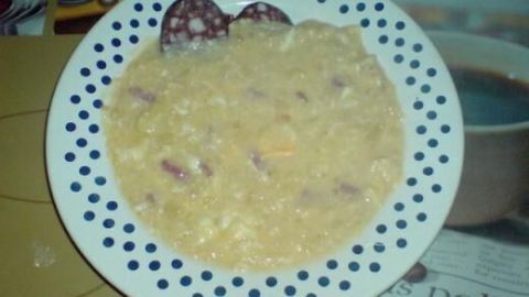 Ein Teller mit süß-saurer Kartoffelsuppe, garniert mit Wurstscheiben, steht auf einem Tisch mit Zeitschriften als Unterlage.