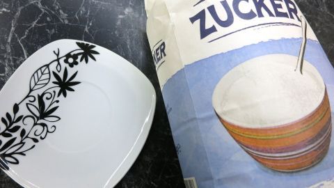 Eine Papiertüte mit Zucker steht neben einem weißen Teller mit floralem Design, bereit für eine süße Wespenfalle.