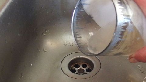 Abfluss durch Kerzenwachs verstopft? Die einzige Lösung ist: U-Rohr abschrauben und festen Wachsklumpen wieder entfernen. Ein Glas wird über einen Abfluss gehalten, während Wasser darauf zugießt, um eine Verstopfung durch Kerzenwachs zu lösen.