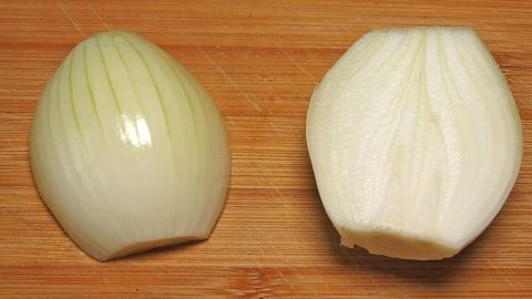 Eine geschnittene Zwiebel liegt auf einem Holzbrett, bereit zum Kochen, während sie durch den Schnitt frische Aromen entfaltet.