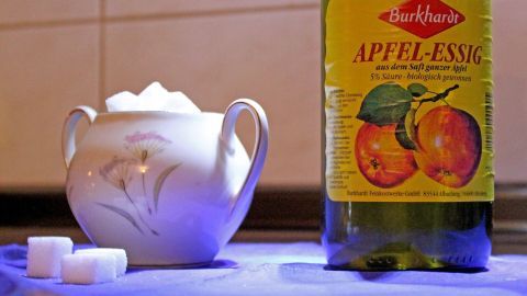 Ein Stück Würfelzucker mit Apfelessig kann den Schluckauf beseitigen. Ein Porzellanbehälter mit Würfelzucker steht neben einer Flasche Apfelessig auf einer Arbeitsfläche in einer Küche.