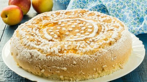 Ein saftiger Ei-Schwer-Kuchen liegt auf einem weißen Teller, umgeben von frischen Äpfeln und einem blauen Tuch.