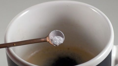 Aromatischeren Kaffee erhält man, wenn dem Kaffeepulver, eine Prise Salz zugegeben wird Eine Teelöffel mit Salz schwebt über einer Tasse Kaffee, bereit, den Geschmack durch das Hinzufügen von Salz zu verbessern.
