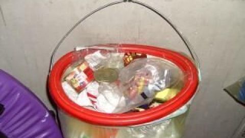 Ein gefüllter gelber Sack hängt an einem Haken in einem Kellerraum. Er enthält Plastikmüll und Verpackungen.