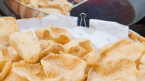 Knusprige Krabbenchips liegen auf einem Teller, während im Hintergrund eine Pfanne mit heißem Öl zum Frittieren bereitsteht.