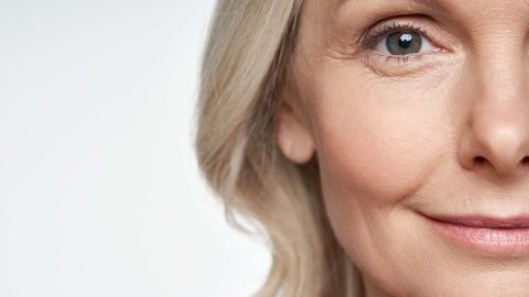 Ein älterer Mensch mit sanften Gesichtsfalten lächelt, umgeben von hellem, neutralem Hintergrund, was eine freundliche Ausstrahlung schafft.