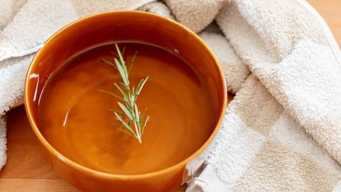 Eine helle Schüssel mit Dampfbad, gefüllt mit warmem Wasser und einem Zweig, steht auf der Holzoberfläche, um Mitesser zu bekämpfen.
