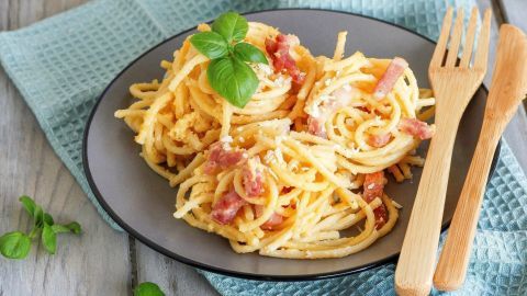 Ein Teller fettarme Carbonara-Sauce mit Spaghetti und Basilikum, schön angerichtet auf einem blauen Tuch.