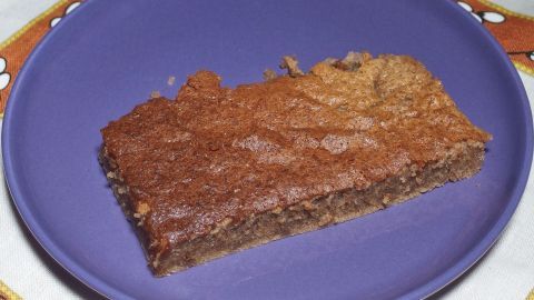 Ein Stück Schokoladenkuchen auf einem lila Teller liegt auf einem hellen Tisch, umgeben von einer gemütlichen Atmosphäre.