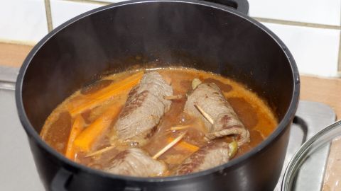 Im Rouladentopf garen saftige Rinderrouladen zusammen mit Karotten in einer aromatischen Brühe auf dem Herd.