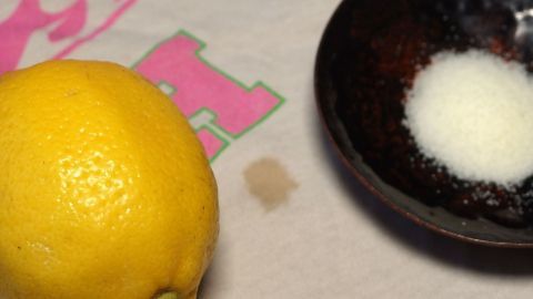 Ein Zitrone liegt neben einer Sch&uuml;ssel mit Zucker auf einem Kleidungsst&uuml;ck mit Rostflecken.