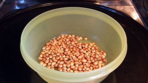 In einer grünen Schüssel befinden sich ungepopte Maiskörner, die zum Zubereiten von Mikrowellenpopcorn vorgesehen sind.