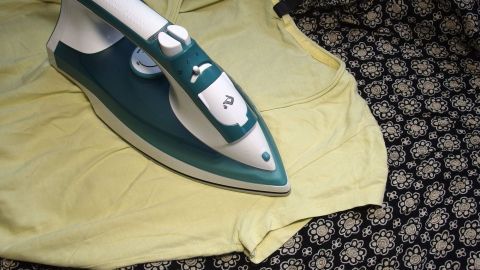 Ein Bügeleisen liegt auf einem gelben T-Shirt, während es mit Dampf bearbeitet wird, um Klebeflecken zu entfernen.