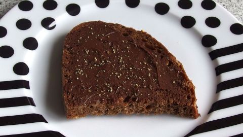 Ein Stück Nutellabrot liegt auf einem kontrastierenden, gestreiften Teller und ist mit Pfeffer bestreut.