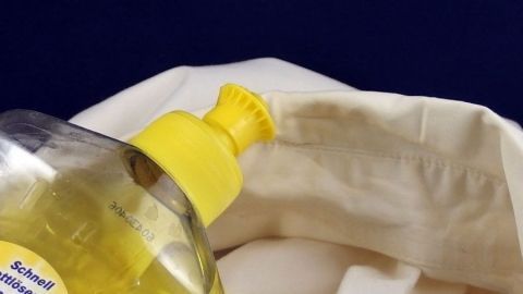 Eine Flasche mit gelbem Deckel steht nahe einem weißen Hemd, während Reinigungsmittel für das Entfernen von Kragenspeck verwendet wird.