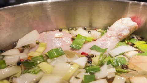 Hühnersuppe köchelt in einem großen Topf, während Gemüse und Gewürze im Wasser garen und Aromen entwickeln.