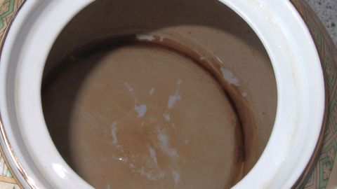 Mit Cola braune Beläge von Tee in Tassen entfernen. Eine braune Teetasse mit Cola steht auf einer Arbeitsfläche, während sie gereinigt wird, um Ablagerungen zu entfernen.