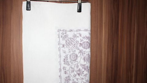Ich hänge meine Tischdecken so in meinen Kleiderschrank und habe immer glatte faltenfreie Tischwäsche. Ein weißes Tischtuch hängt an einer Wäscheleine, sorgfältig gefaltet, um Knickfalten nach dem Bügeln zu vermeiden.