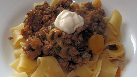 Eine Portion Hackfleisch-Lauch-Topf ruht auf einem Bett aus Nudeln, garniert mit einem Klecks Sauerrahm.