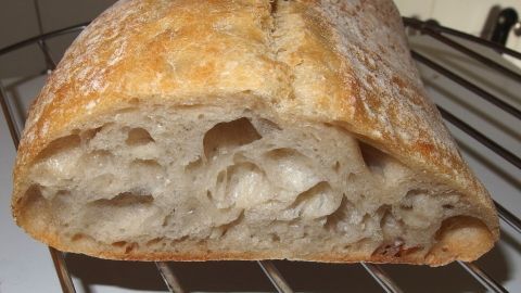 Ein frisch gebackenes Ciabattabrot liegt auf einem Gitterrost, bereit zum Servieren mit gegrilltem Essen.