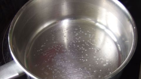 Ein kochender Topf mit Wasser zeigt Kalkflecken am Boden nach dem Eierkochen, auf einem Herd in einer Küche.