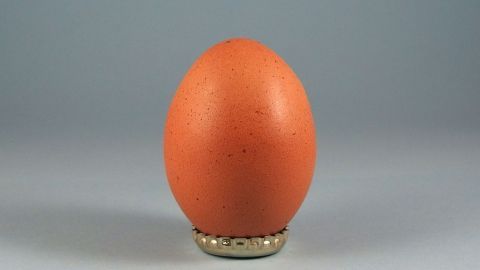 Ein Behelfs-Eierbecher hält ein braunes Ei stabil, präsentiert vor einem neutralen Hintergrund.