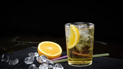 Ein Glas mit Wodka und Eiswürfeln, verziert mit Zitronenscheiben, steht neben einer halbierten Orange auf einem dunklen Untergrund.