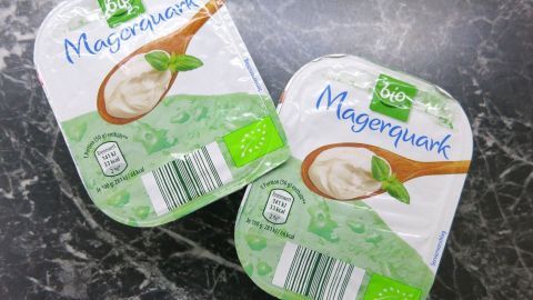 Ein effektives, schmerzlinderndes Hausmittel gegen Schwellungen und Entzündungen ist der allbekannte Quark. Zwei Packungen Magerquark liegen auf einer dunklen, marmorierten Oberfläche, bereit zur Anwendung gegen Schwellungen.